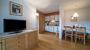 Una cocina moderna con armarios de madera, un comedor con mesa y sillas, un televisor sobre un mueble y luminarias colgantes.