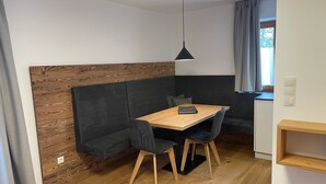 Una stanza compatta con un tavolo da pranzo in legno, un divano scuro e un angolo cottura piccolo.