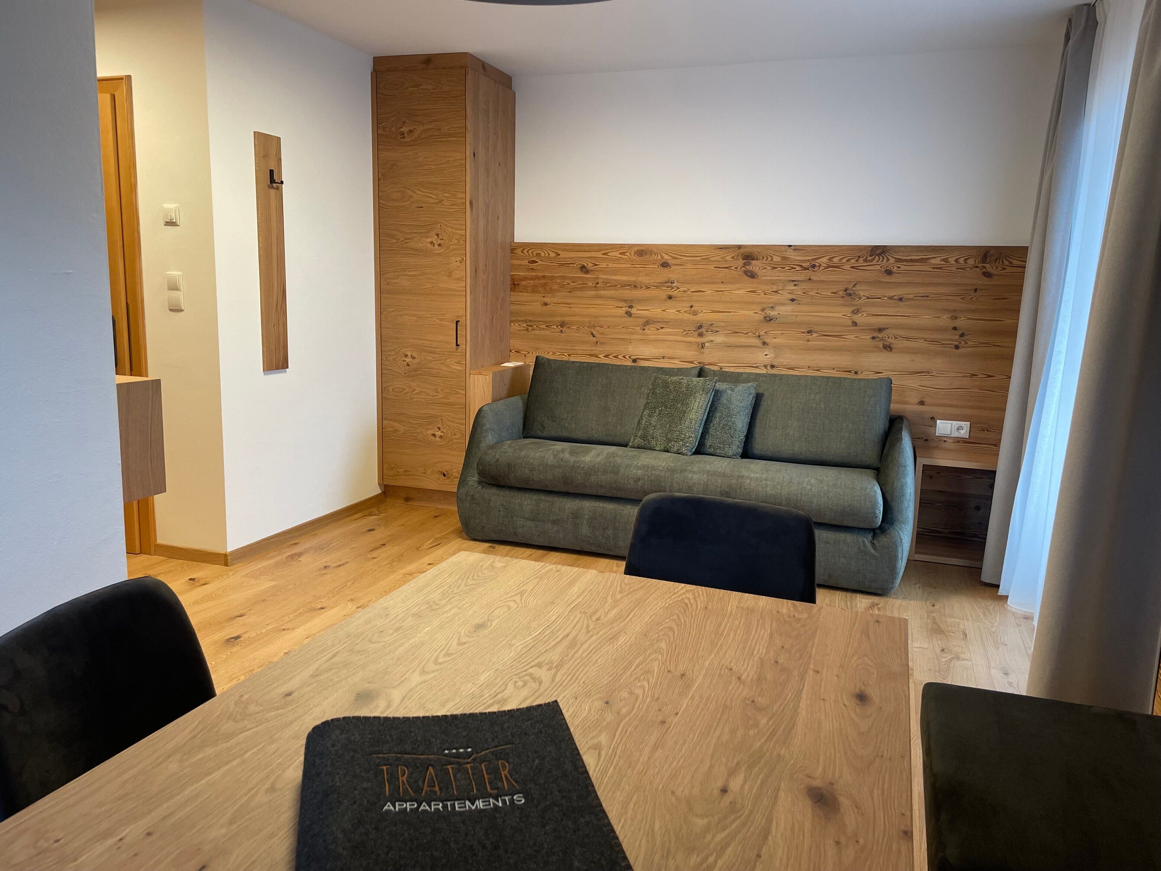 Een moderne woonkamer met een houten accentmuur, een grijze bank en een houten eettafel.