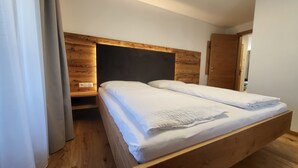 Un letto singolo con un poggiatesta in legno, un comodino, un pavimento in legno e una porta sulla destra.