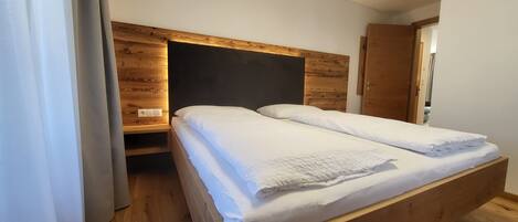 A single bed with a wooden headboard and a bedside table, a wooden floor, and a door to the right.
