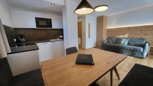 Una cucina moderna con mobili bianchi, un forno a microonde e una macchina da caffè. C'è un tavolo da pranzo in legno con un sottopiattino, un divano grigio e una parete d'accento in legno.