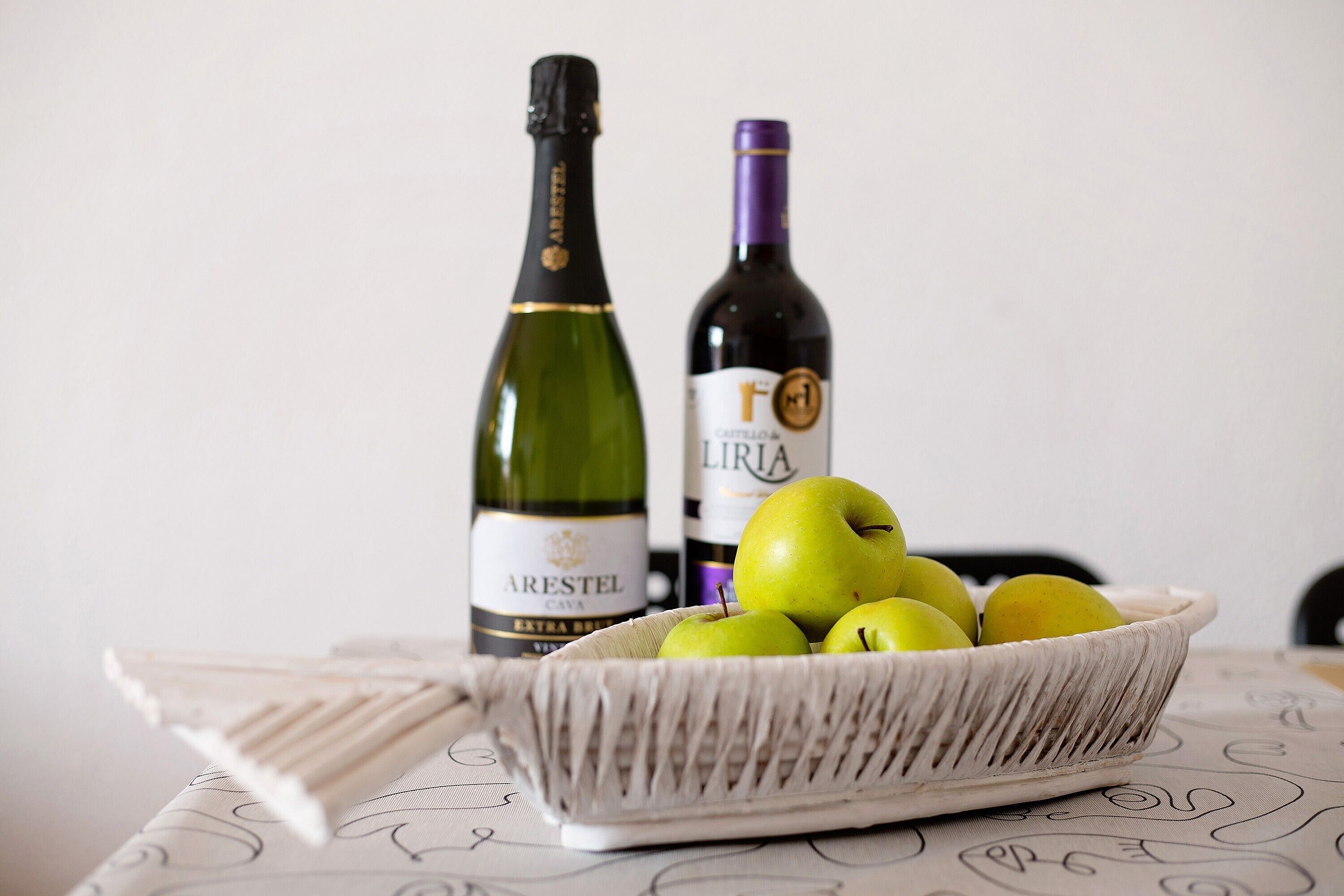 Une bouteille de vin Arestel, une autre bouteille de vin et un panier de pommes vertes sur une table.