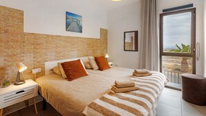 Ein Hotelzimmer mit einem großen Bett, einem Nachttisch mit Lampe, einem Fenster mit Blick und einer Backsteinwand.