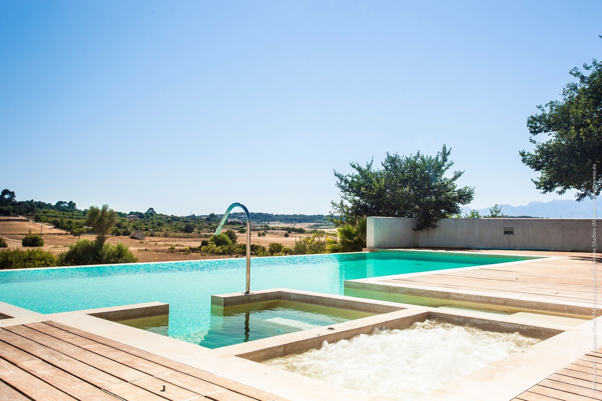 Een zwembad met een houten terras, een jacuzzi en uitzicht op het landschap.