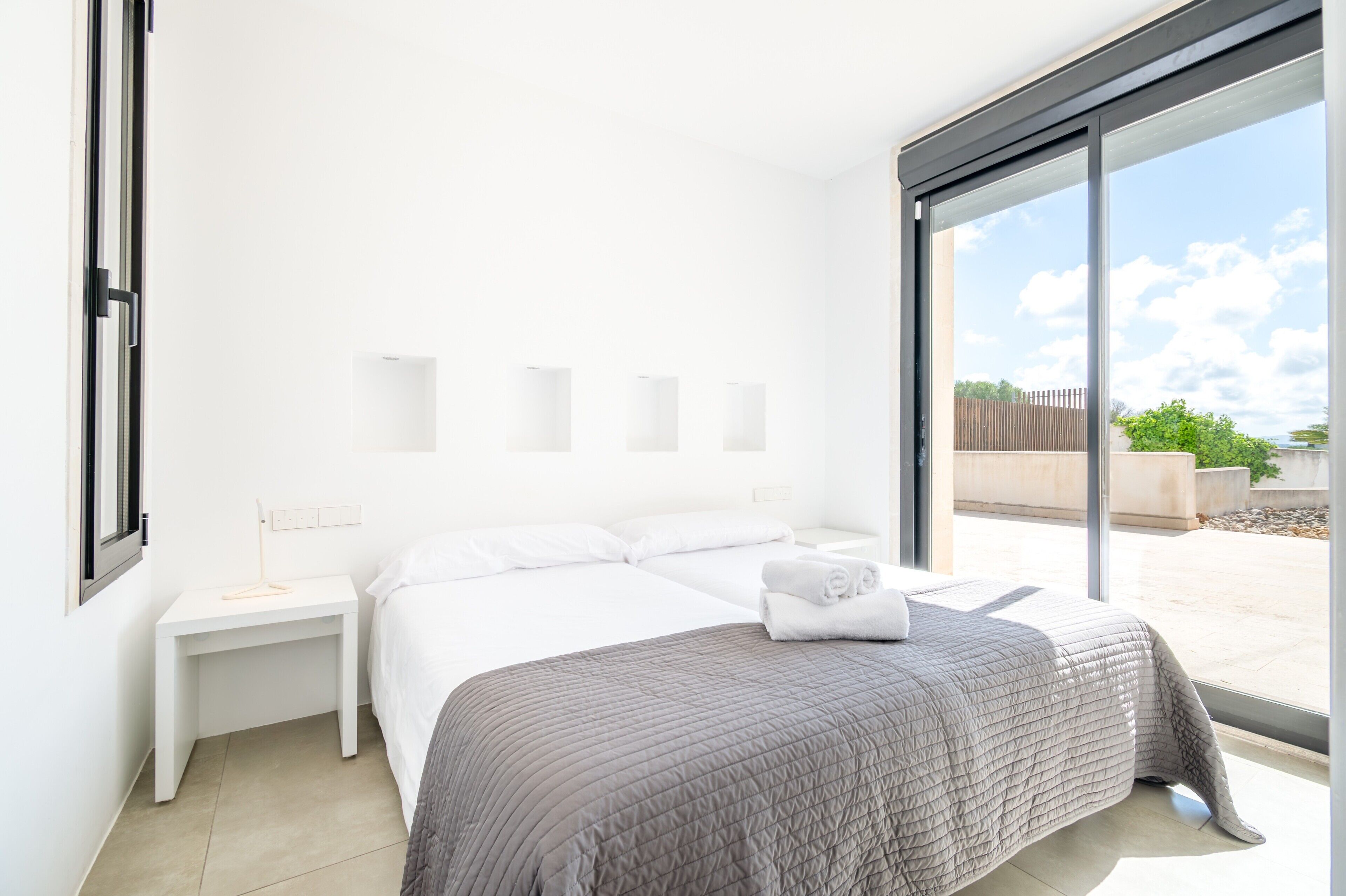 Una habitación de hotel moderna con una cama grande, una mesita de noche y vistas a través de un ventanal corredero.