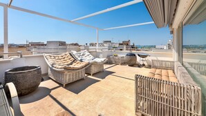 Terraza en la azotea con mobiliario de mimbre, una maceta de piedra grande y vistas a la ciudad.