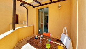 A balcony with a wooden table, a white bag, and a glass door leading to an interior space.