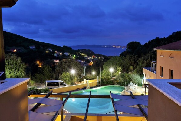 A pool area with a view of a coastal town at dusk.