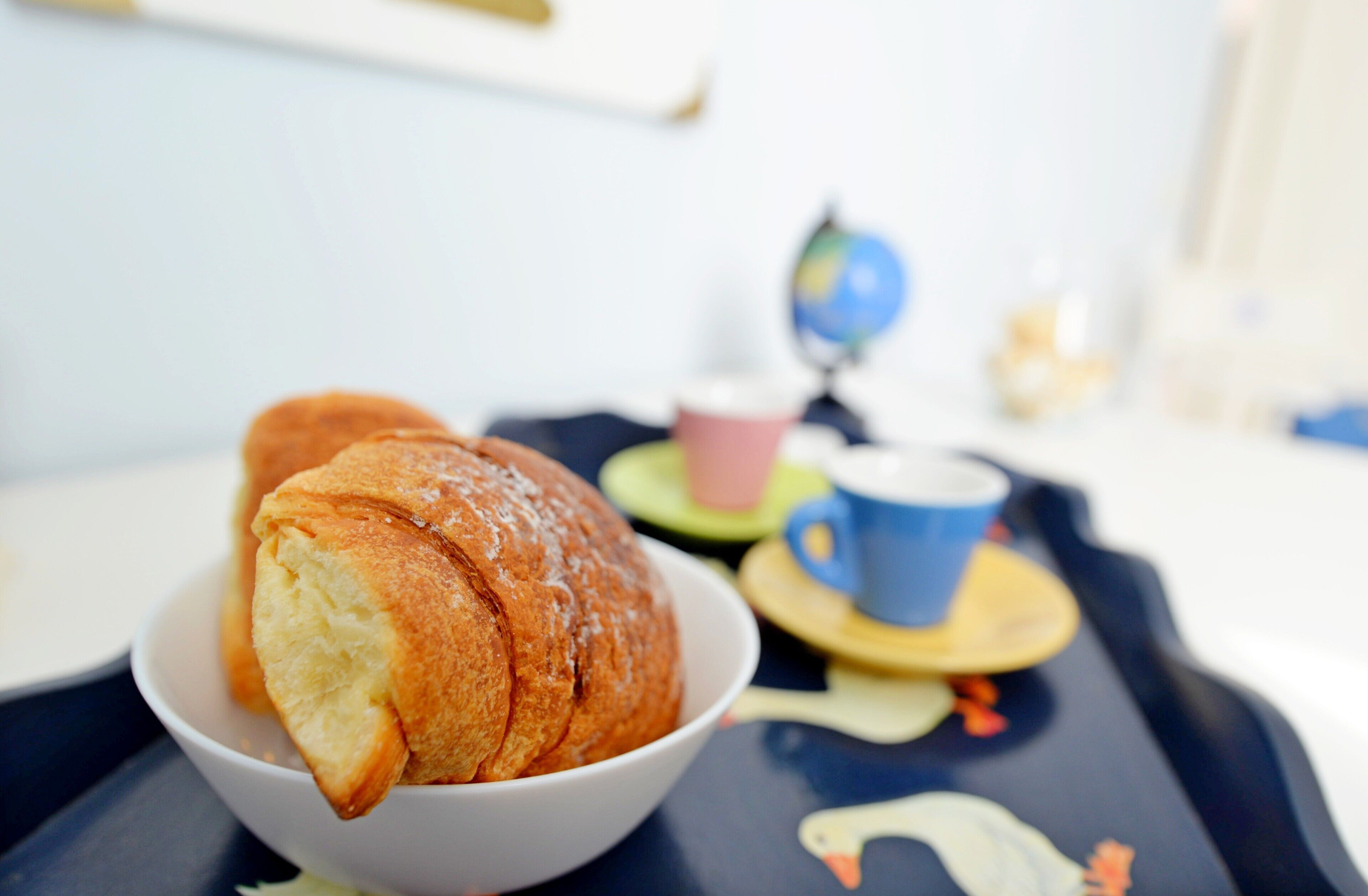 Una mesa con un bol de pan, una taza y un globo terráqueo.