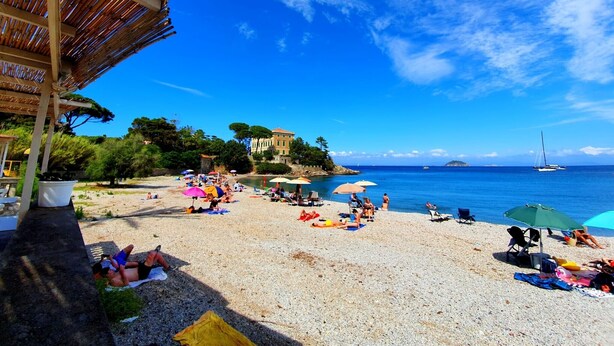 A beach with umbrellas, people sunbathing, and a building in the background.