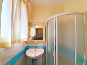 Un baño con lavamanos, espejo, ducha y perchero para toallas.