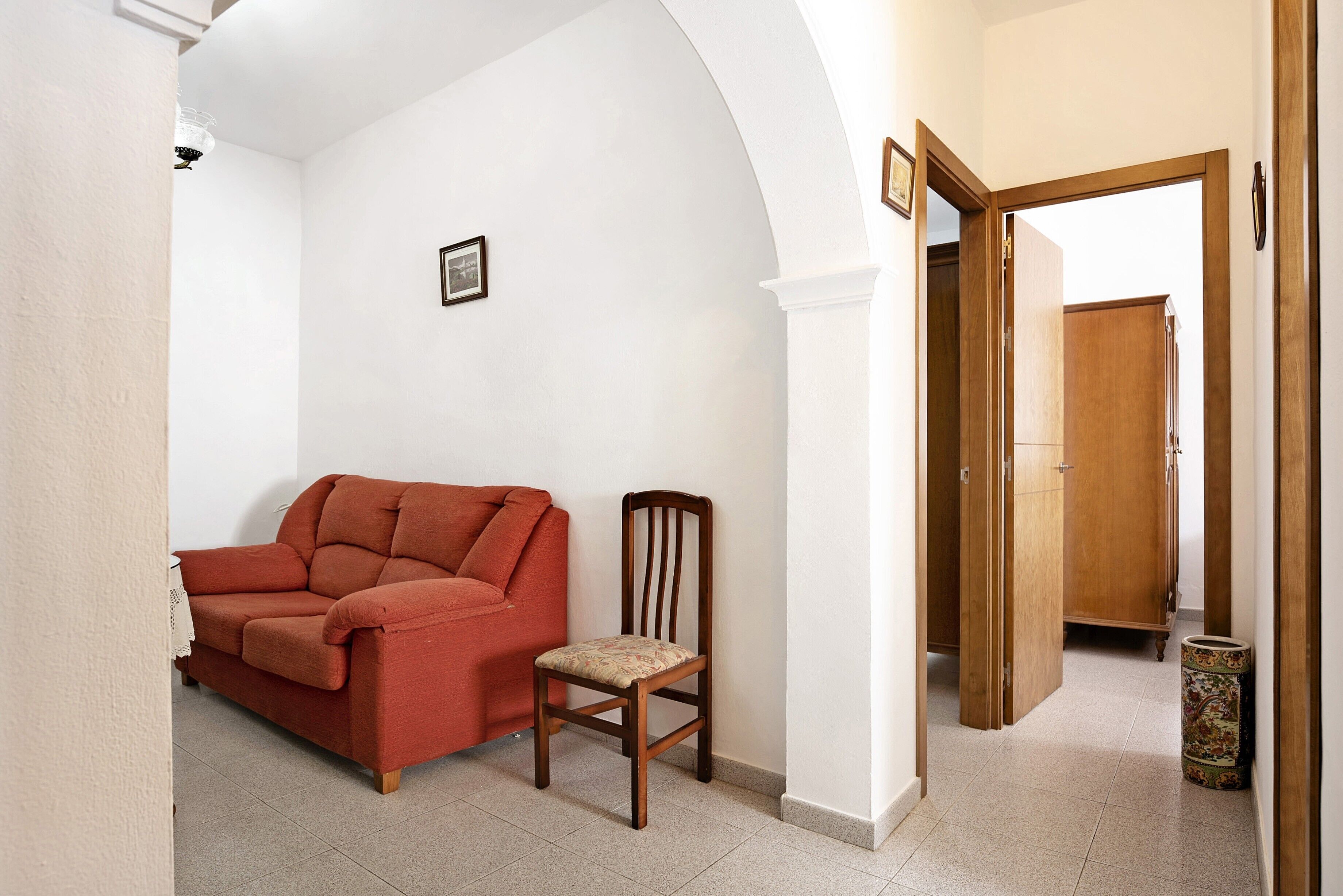A living room with a red sofa, a wooden chair, and a wooden cabinet.