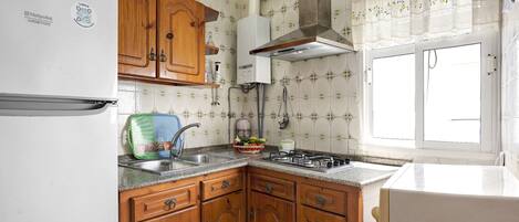 A kitchen with wooden cabinets, a white refrigerator, a gas stove, and a window with a view.