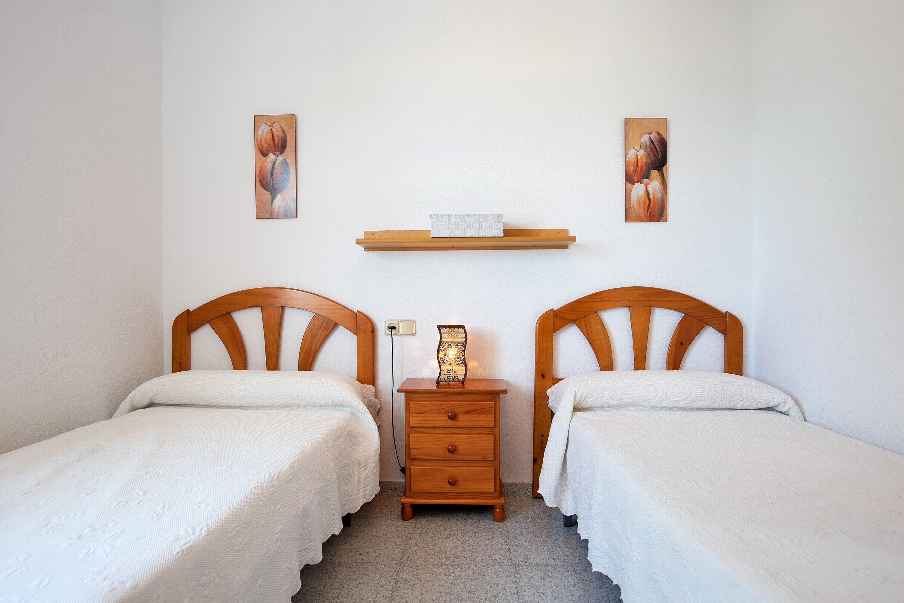 Une chambre à coucher avec deux lits en bois, une table de chevet avec une lampe et une étagère où sont exposées des œuvres d’art.