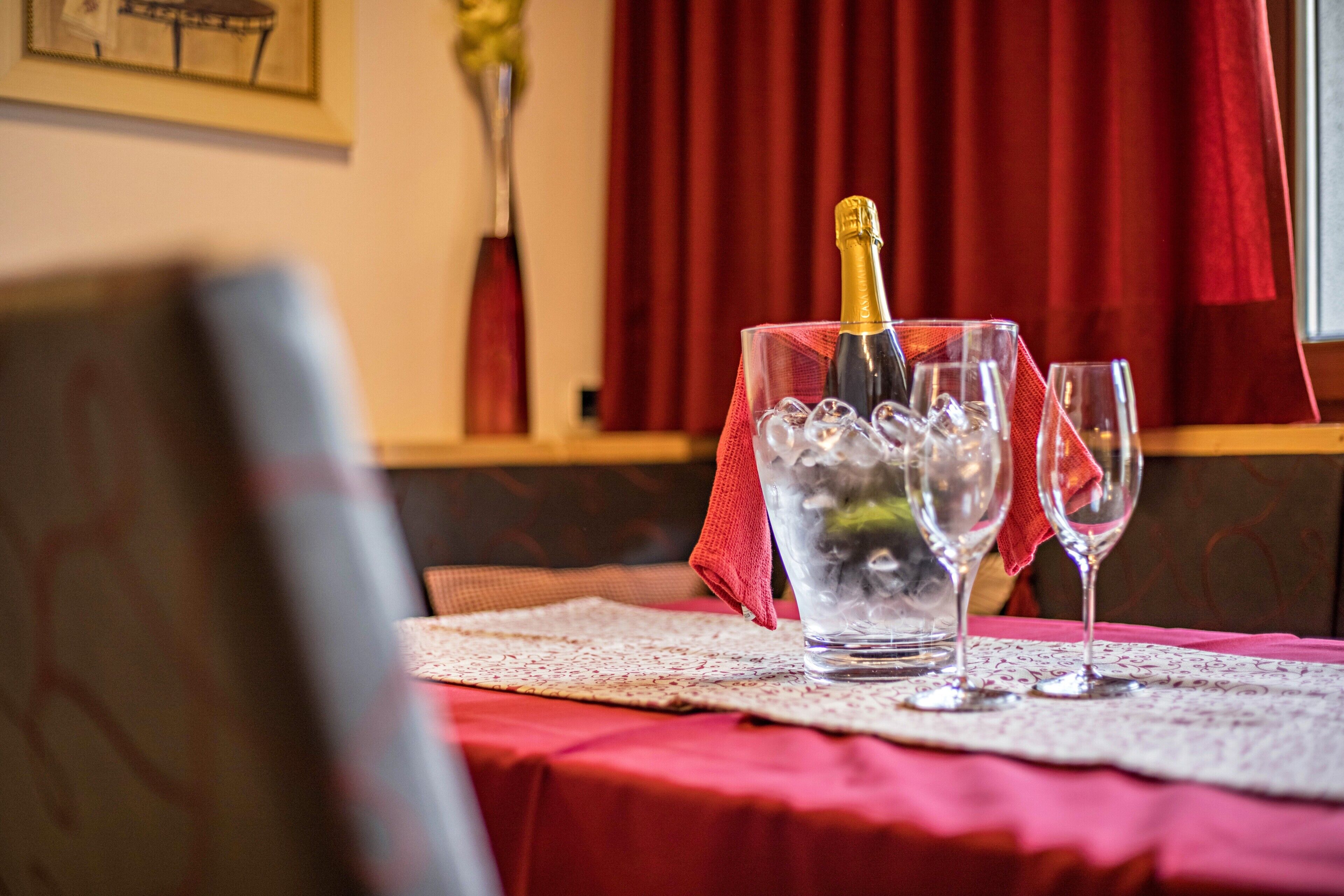 Ein Tisch mit einer Champagnerflasche, Eiswürfeln und zwei Gläsern auf einer roten Tischdecke.