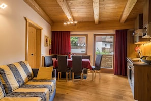 Une pièce chaleureuse avec un plafond en bois, un canapé, une table à manger avec des chaises et un coin cuisine.