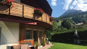 A wooden building with a balcony, a patio with seating, and a view of a mountainous landscape. - Pet-friendly Apartment "Villa Anita Pares" with Mountain View, Sauna, Wi-Fi, Terrace & Balcony (St.Vigil)
