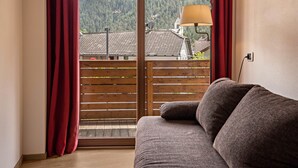 A room with a wooden floor, a grey sofa, a window with red curtains, and a view of a mountain. - Pet-friendly Apartment "Villa Anita Pares" with Mountain View, Sauna, Wi-Fi, Terrace & Balcony (St.Vigil)