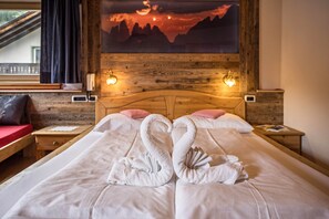 Une chambre d’hôtel avec un lit agrémenté de deux serviettes disposées en forme de cygnes, une tête de lit en bois, un tableau représentant un coucher de soleil et une fenêtre avec des rideaux.