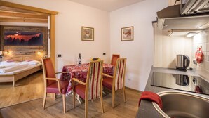 A compact room with a bed, a dining table with chairs, a kitchen area with a sink, and a wall-mounted TV. - Pet-friendly Apartment "Villa Anita Pares" with Mountain View, Sauna, Wi-Fi, Terrace & Balcony (St.Vigil)