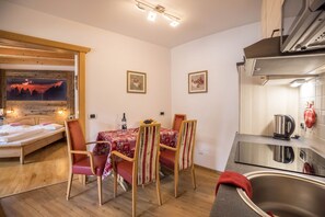 Una stanza compatta con un letto, un tavolo da pranzo con sedie, un angolo cottura con lavandino e una TV a parete.
