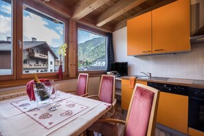A kitchen with wooden cabinets, a dining table with chairs, a TV, and a view of a mountain.