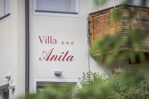 Un bâtiment sur lequel on peut lire l’inscription « Villa Anita », et une fenêtre dotée d’un volet en bois.