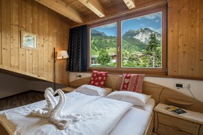 A wooden-paneled room with a bed, a nightstand, a lamp, and a window with a mountain view.