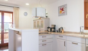 A kitchen with white cabinets, a coffee maker, and a clock on the wall.