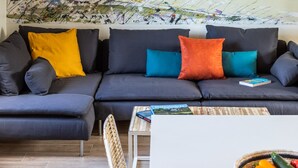 Un soggiorno moderno con un divano grigio scuro, cuscini colorati, un tavolino da caffè bianco e un grande quadro astratto appeso alla parete.
