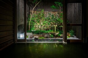 A traditional Japanese interior with a wooden door, a stone wall, and a small water feature. - Suigetsu Machiya House (Kyoto)