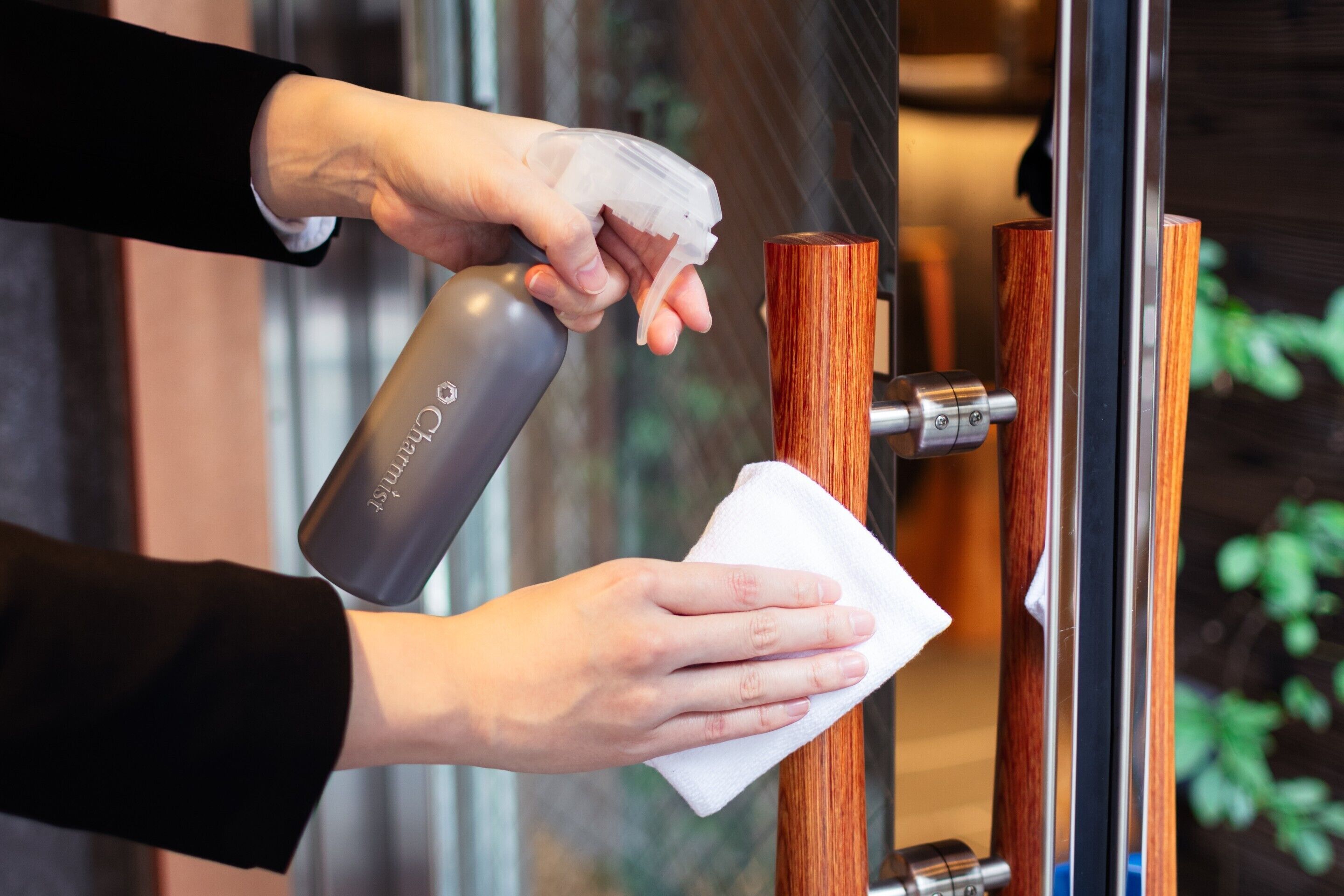 A person cleaning a wooden door handle with a cloth and a spray bottle.