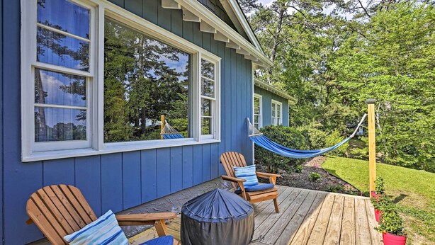 Una terrazza con due sedie di legno e un'amaca, una casa blu con ampie finestre e un'altra terrazza in legno.