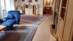 A living room with a blue leather sofa, two large rugs, wooden cabinets, and a television. - Ferienhaus am Rheintor (Andernach)