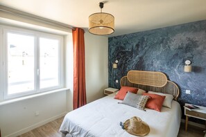 A bedroom with a bed, a window with curtains, a wall-mounted lamp, and a textured wall.