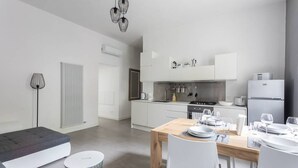 A modern kitchen with white cabinets, a dining table set for four, and a gray sofa in the living area.