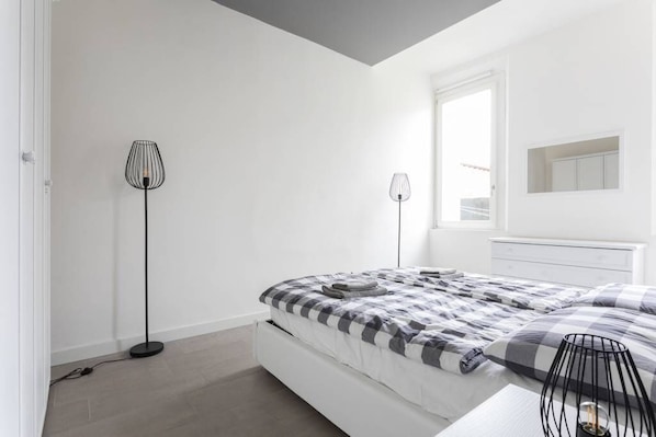 A modern bedroom with a bed, two floor lamps, a window, and a built-in wardrobe.