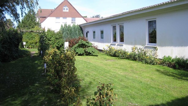 A white building with a red roof, surrounded by a well-maintained lawn and various shrubs. - Apartment for 2 people - Seahorse (Insel Hiddensee)