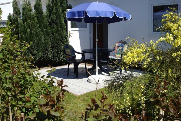 Un patio al aire libre con una sombrilla azul, dos sillas y una pequeña mesa.