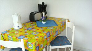 A small dining table with a colorful tablecloth, two white chairs, a coffee maker, and a toaster. - Apartment for 2 people - Seahorse (Insel Hiddensee)