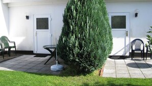 A building with two doors, a small table, two chairs, and a large evergreen tree in front. - Apartment for 2 people - Seahorse (Insel Hiddensee)