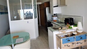 A compact kitchen with a refrigerator, microwave, and coffee maker. There's a small dining table and a cabinet with drawers. - Costa Azahar LEK (Peñiscola)