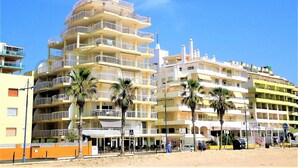 A multi-story hotel with balconies, palm trees, and a sandy beach in the foreground. - Costa Azahar LEK (Peñiscola)