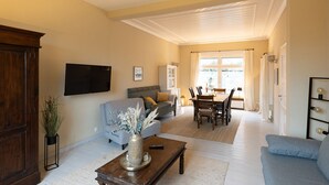 A living room with a sofa, a coffee table, and a TV. There is a dining area with a table and chairs.