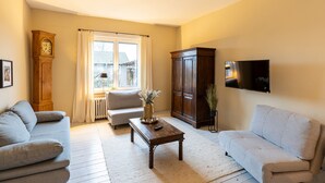 A living room with a sofa, a coffee table, a clock, a cabinet, and a TV.