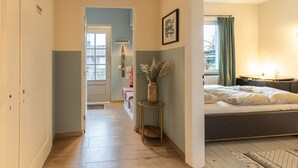 A hallway leading to a bedroom with a bed, a small table with a vase, and a coat rack.