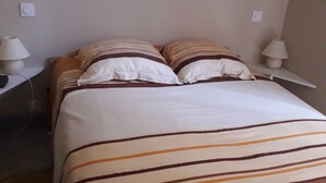 Una cama bien hecha con ropa de cama a rayas, dos lámparas de noche y una pared lisa con un cuadro pequeño.
