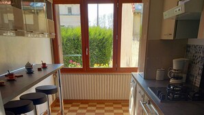 A kitchen with a checkered floor, a bar area with stools, a window with a view of greenery, and a stove. - Maison 4/5 Personnes Avec Jardin Langeais Centre (Langeais)