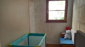 A narrow room with a blue playpen, a small table with a red lamp, and a window with a view of greenery. - Maison 4/5 Personnes Avec Jardin Langeais Centre (Langeais)